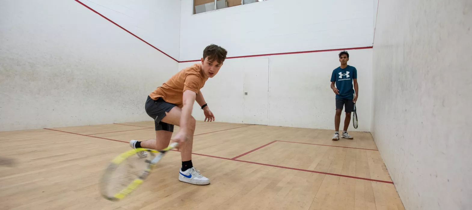 Two students play squash in New College squash courts