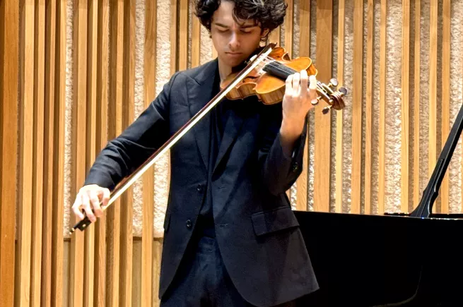 George Lawson playing the violin in a black suit in the New College recital hall.