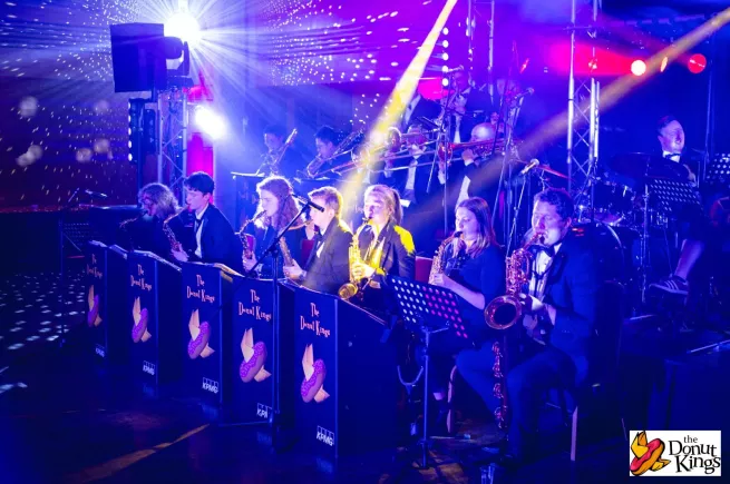 Two rows of brass players perform on colourfully-lit stage.