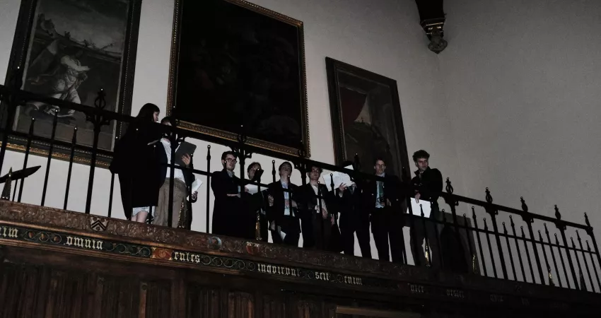 Students singing from a raised platform with paintings behind