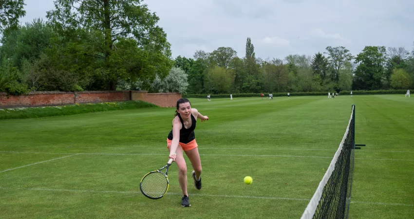 Student plays tennis on grass courts at Weston Sports Ground