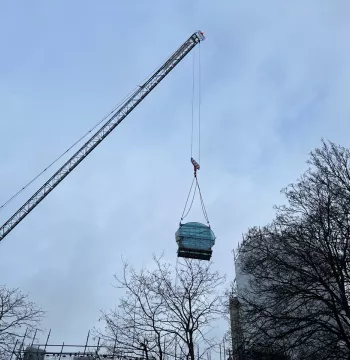 Crane lifting large circular window to top of tower