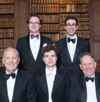 5 men posed in black tie, with shelves of books in the background