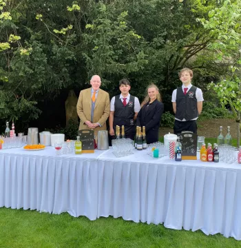 Four people standing behind a table with lots of drinks on