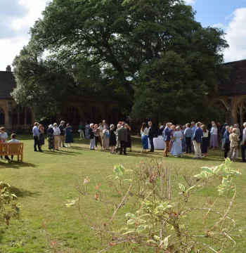 Large group of people on central lawn of some medieval cloisters, with a large oak tree behind